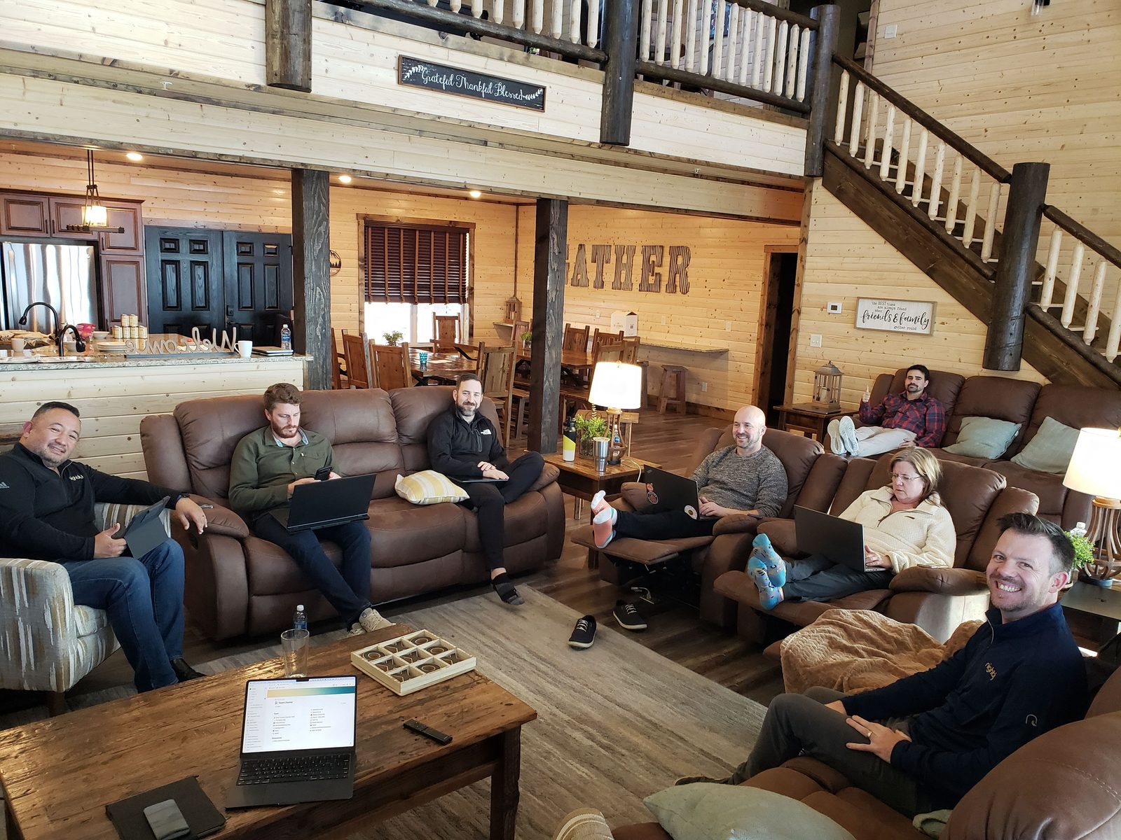 Cohort members with laptops in a relaxed working session inside a timber lodge